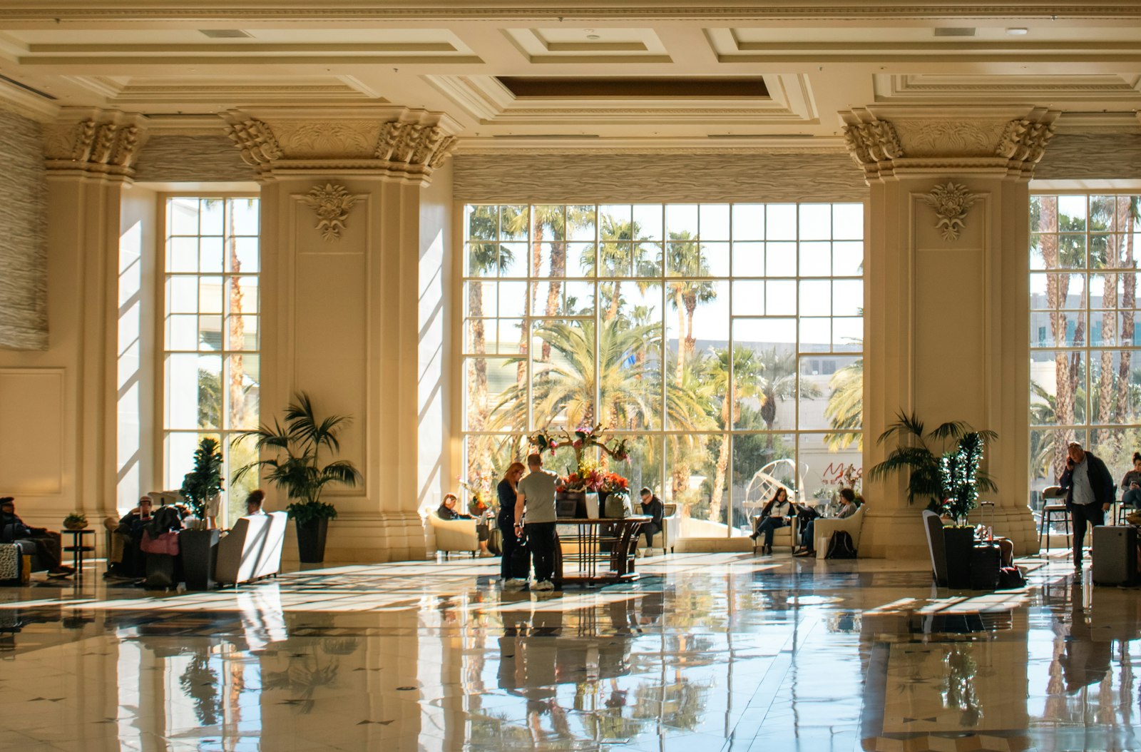 Hall d'un grand hôtel baigné de lumière naturelle, avec des palmiers visibles à travers les baies vitrées